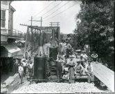Workman gather at the steam-powered concrete mixer during the construction of the Alderson bridge in 1914. Iron bridge is still in place and used as a platforms to pour new bridge abutments, piers, and arches.